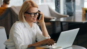 a woman talking on a cell phone while using a laptop